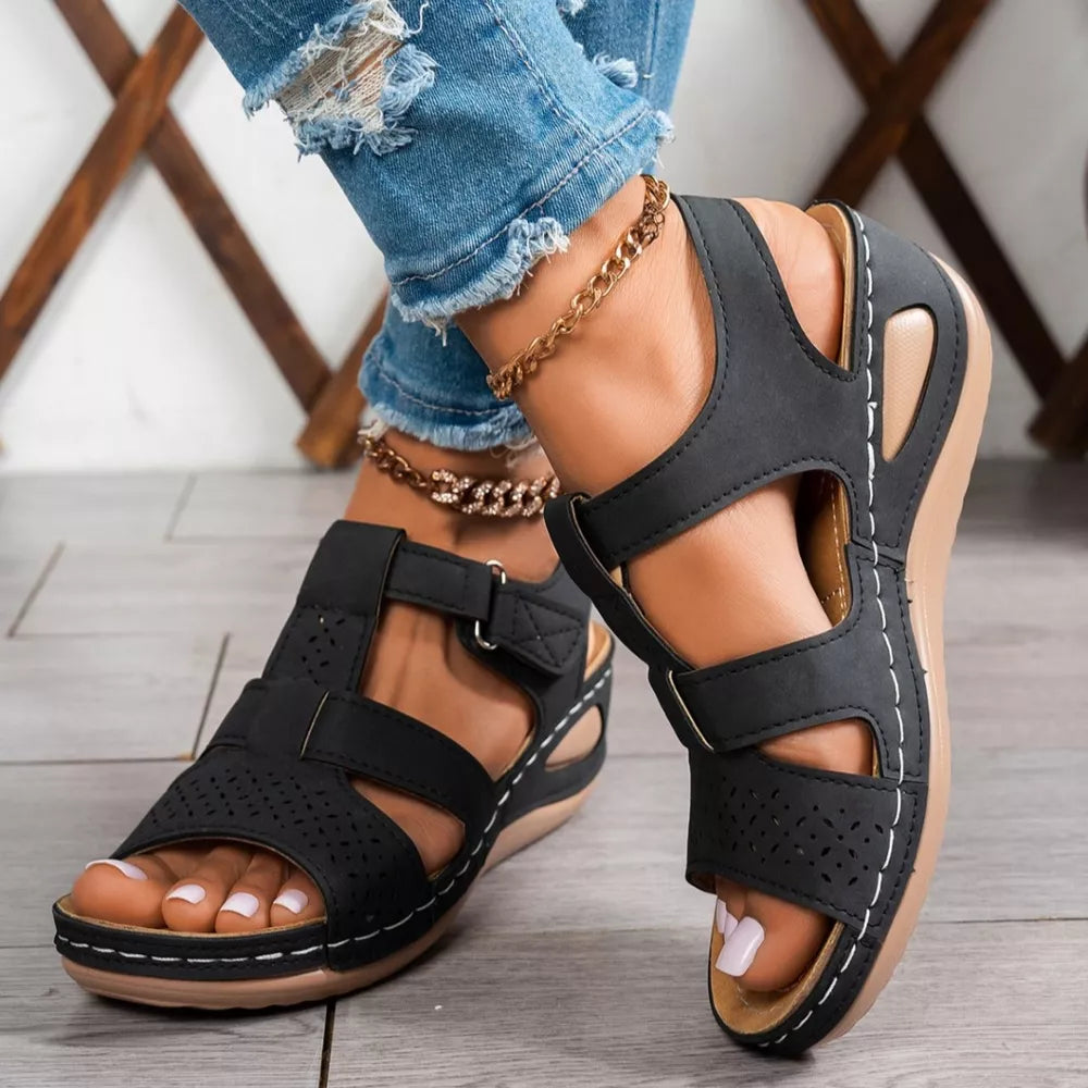 Black perforated mid-wedge sandals with adjustable straps and white stitching detail.