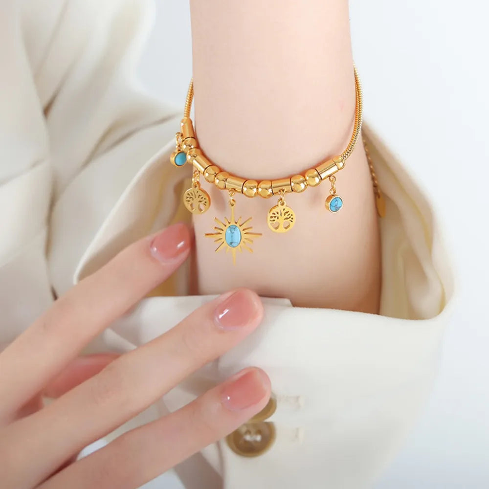 Gold charm bracelet with turquoise accents, featuring sun and tree charms.