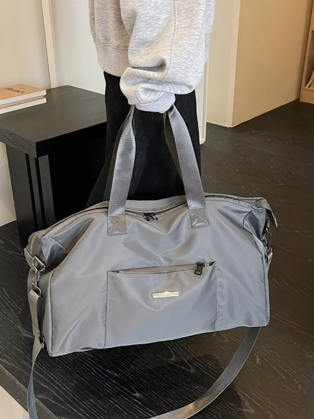 Minimalist grey Oxford cloth travel bag with front zip pocket and shoulder strap.