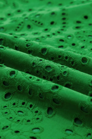 Green cotton eyelet dress fabric with floral cutouts and scalloped hem detail.