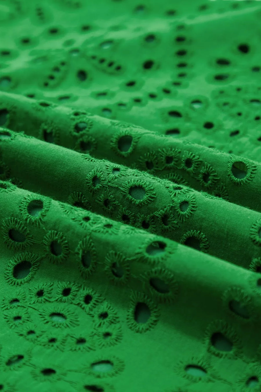 Green cotton eyelet dress fabric with floral cutouts and scalloped hem detail.