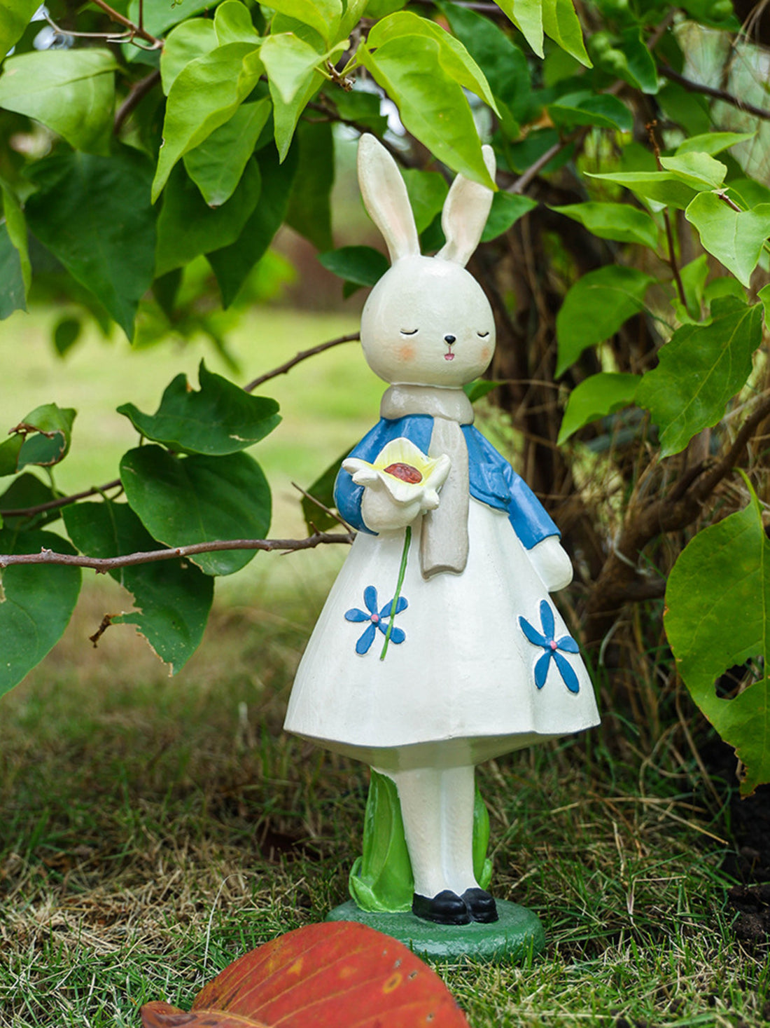 Resin floral rabbit ornament with blue flowers, holding a white flower, wearing a blue jacket and scarf.