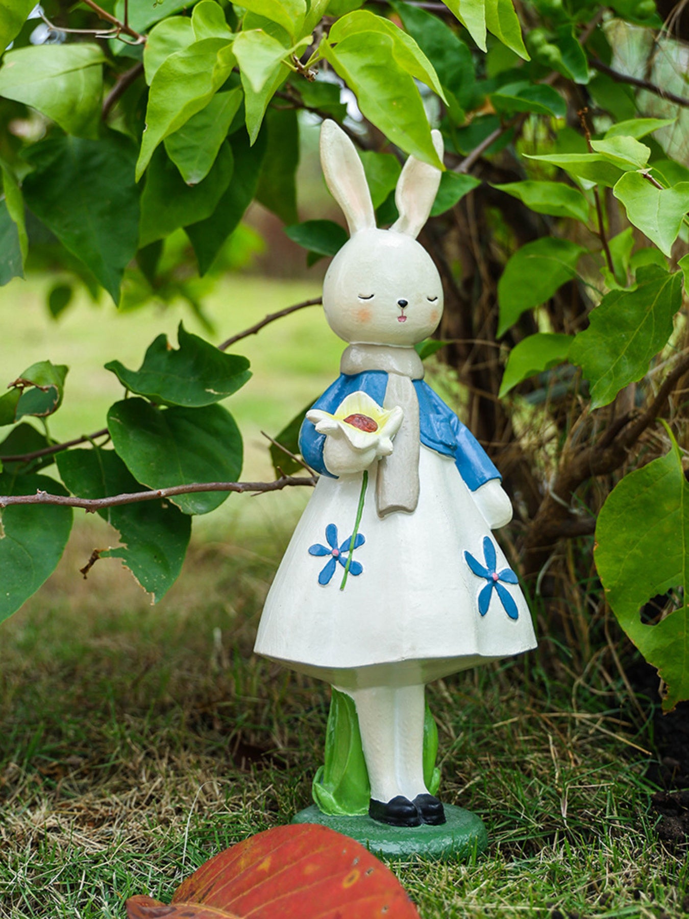 Resin floral rabbit ornament with blue flowers, holding a white flower, wearing a blue jacket and scarf.