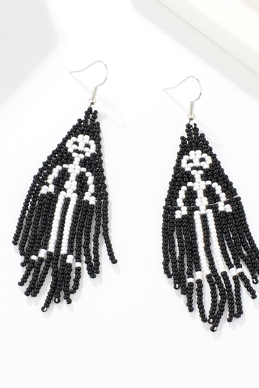 Beaded ghost fringe earrings in black and white with dangling strands.