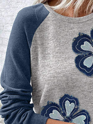 Raglan shirt with blue sleeves and grey body featuring embroidered denim flower patches.