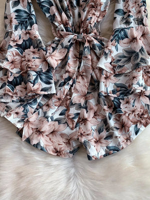 Playful off-shoulder ruffled romper with a floral print and bow detail.