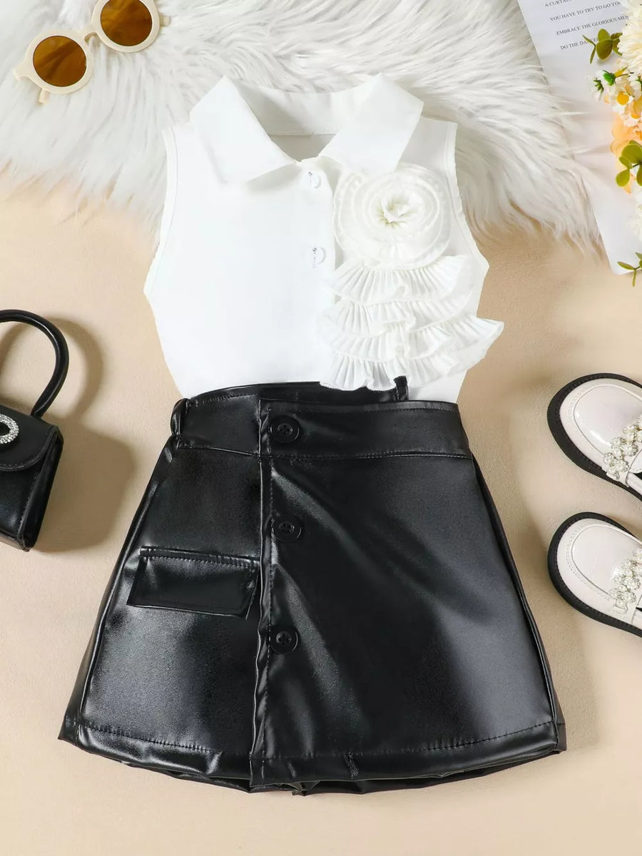Girls' white ruffled top with decorative flower and black faux leather skort.