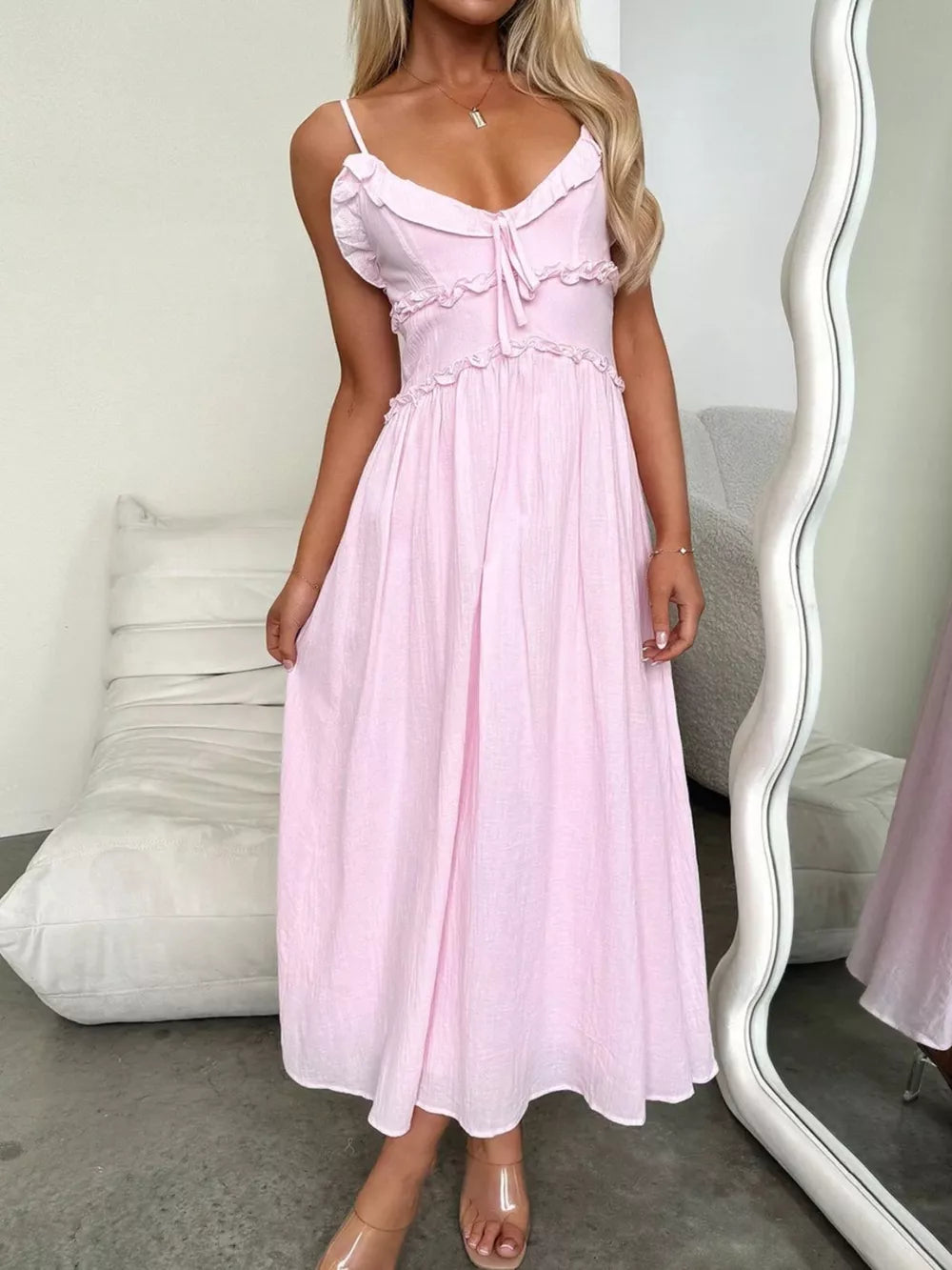 Pink midi dress with spaghetti straps, ruffled neckline, smocked waist, and tie detail.