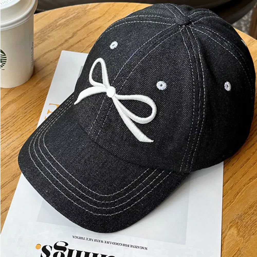 Black baseball cap with white embroidered bow accent and stitching detail.