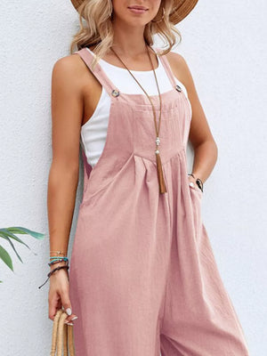 Pink wide-leg romper with adjustable straps and pockets, worn over a white tank top.