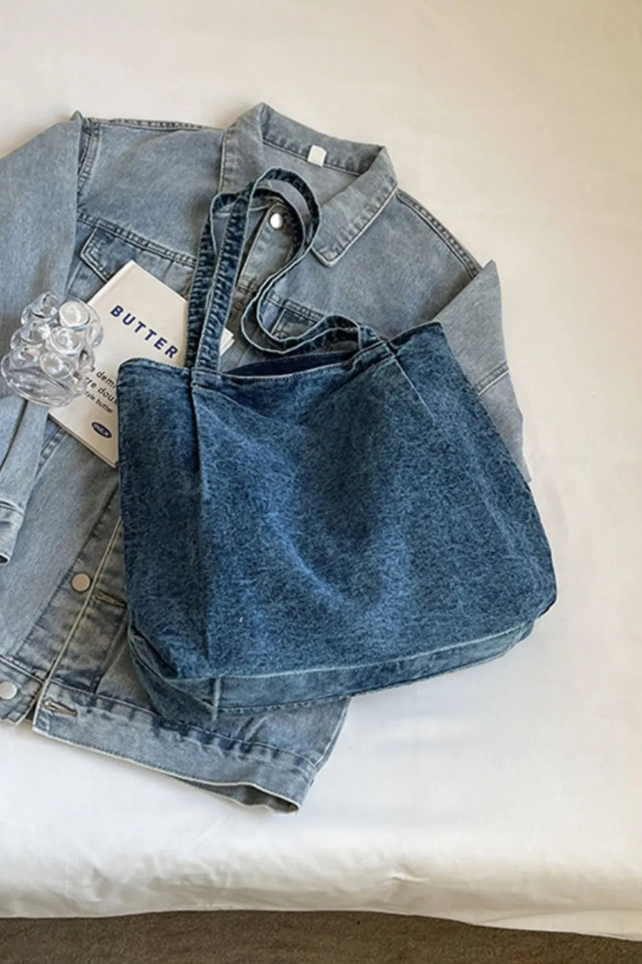 Denim shopper bag with leather trim in dark blue, laid on a denim jacket.