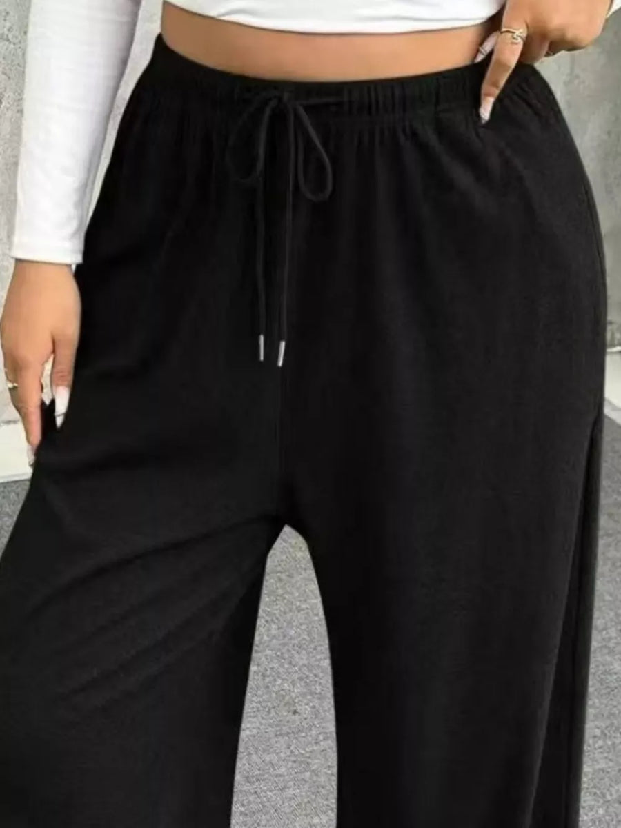 Black drawstring maternity pants with wide legs and side slits.