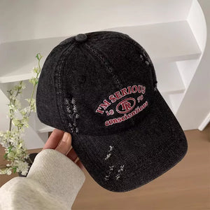Black denim baseball cap with distressed details and red embroidered text.