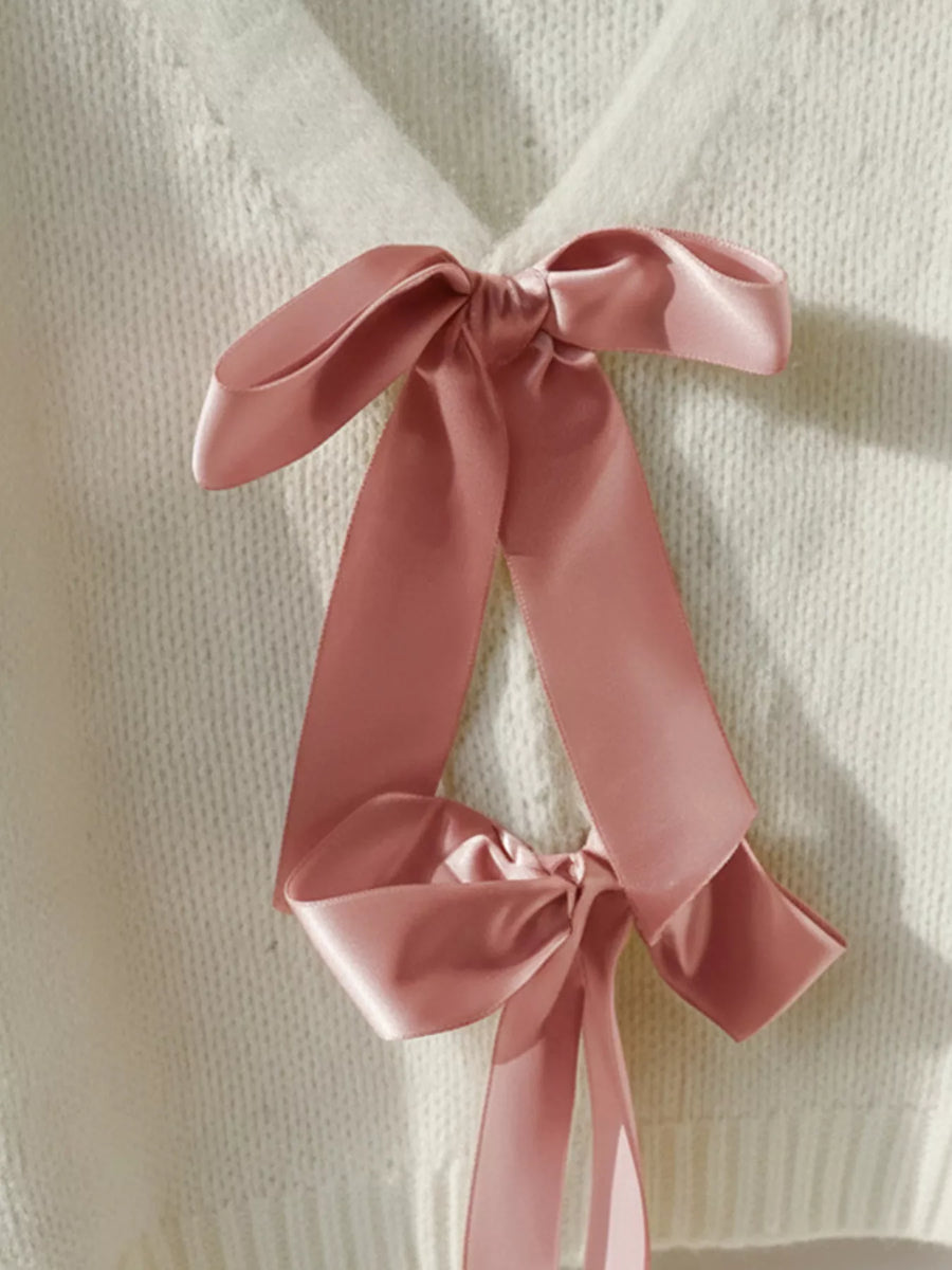 Beige acrylic knit cardigan with pink satin bow embellishments at the V-neck.