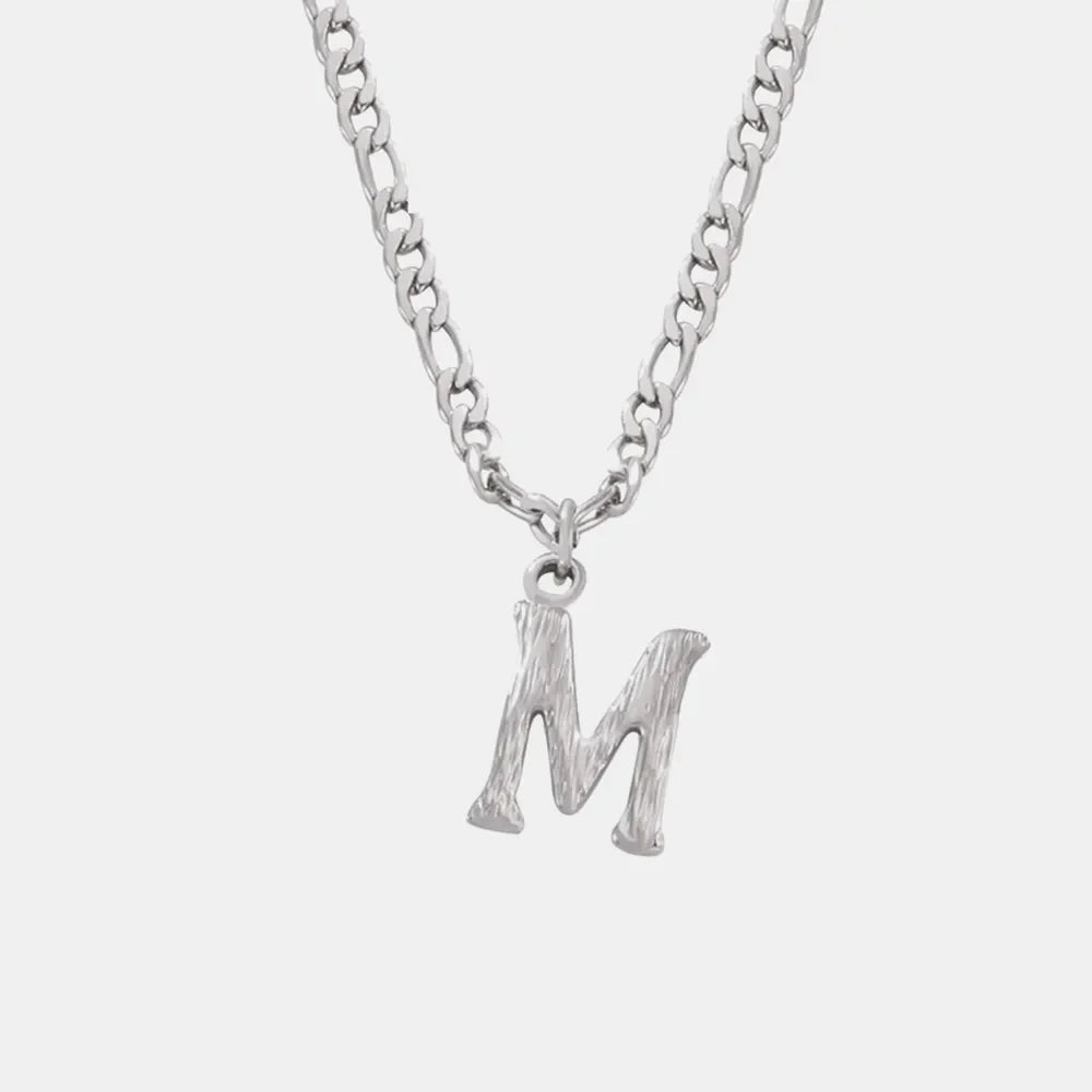 Silver initial pendant necklace with textured letter M on a figaro chain.