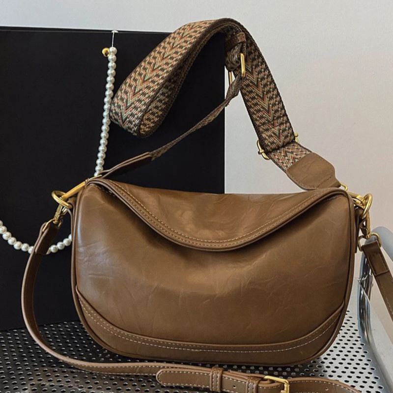 Brown leather crossbody bag with adjustable patterned strap and gold hardware.