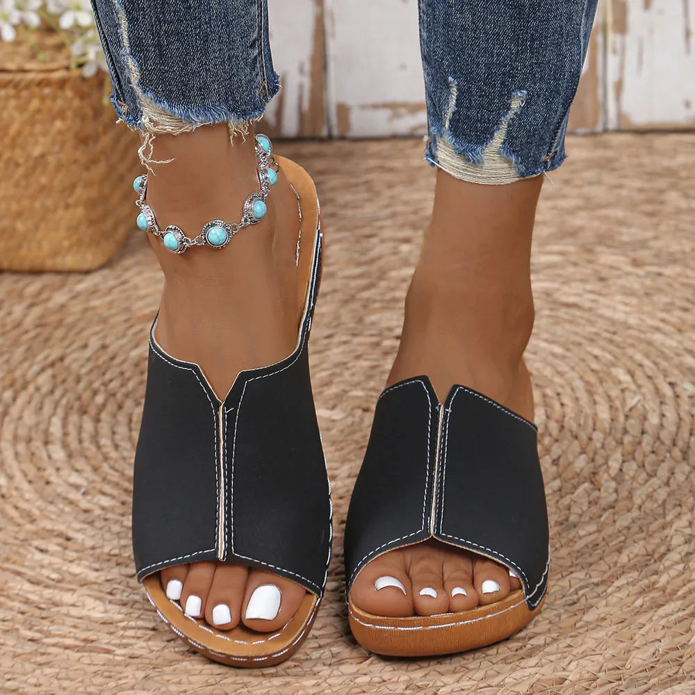 Black wedge mules with white stitching detail and open toe.