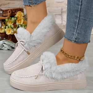 Beige suede loafers with shearling trim and decorative tie detail.