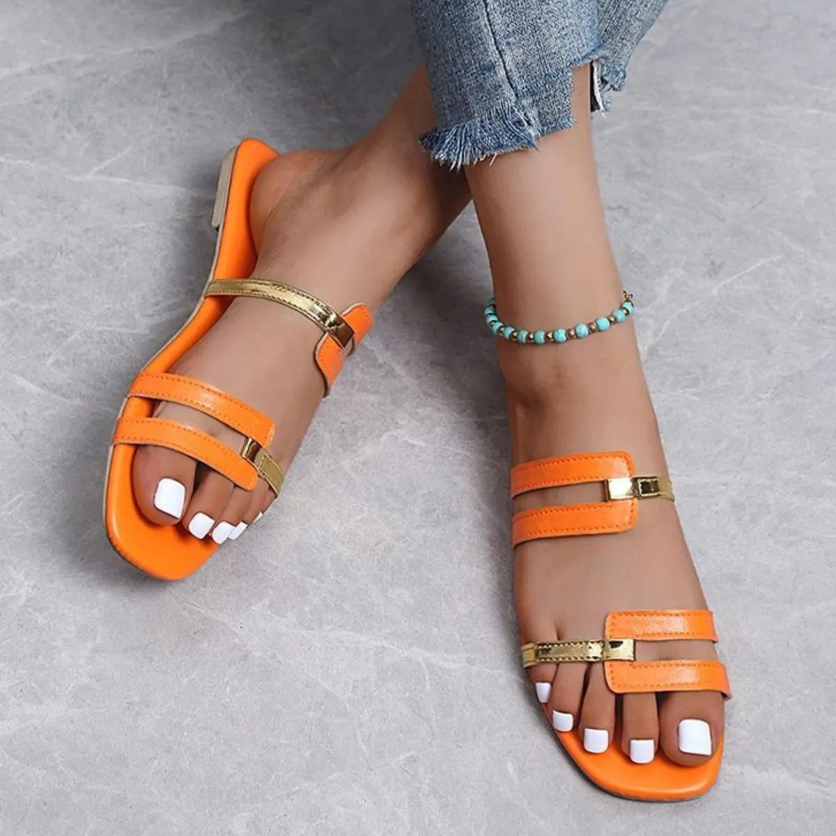 Orange flat slides with gold metallic accent straps and square toe.