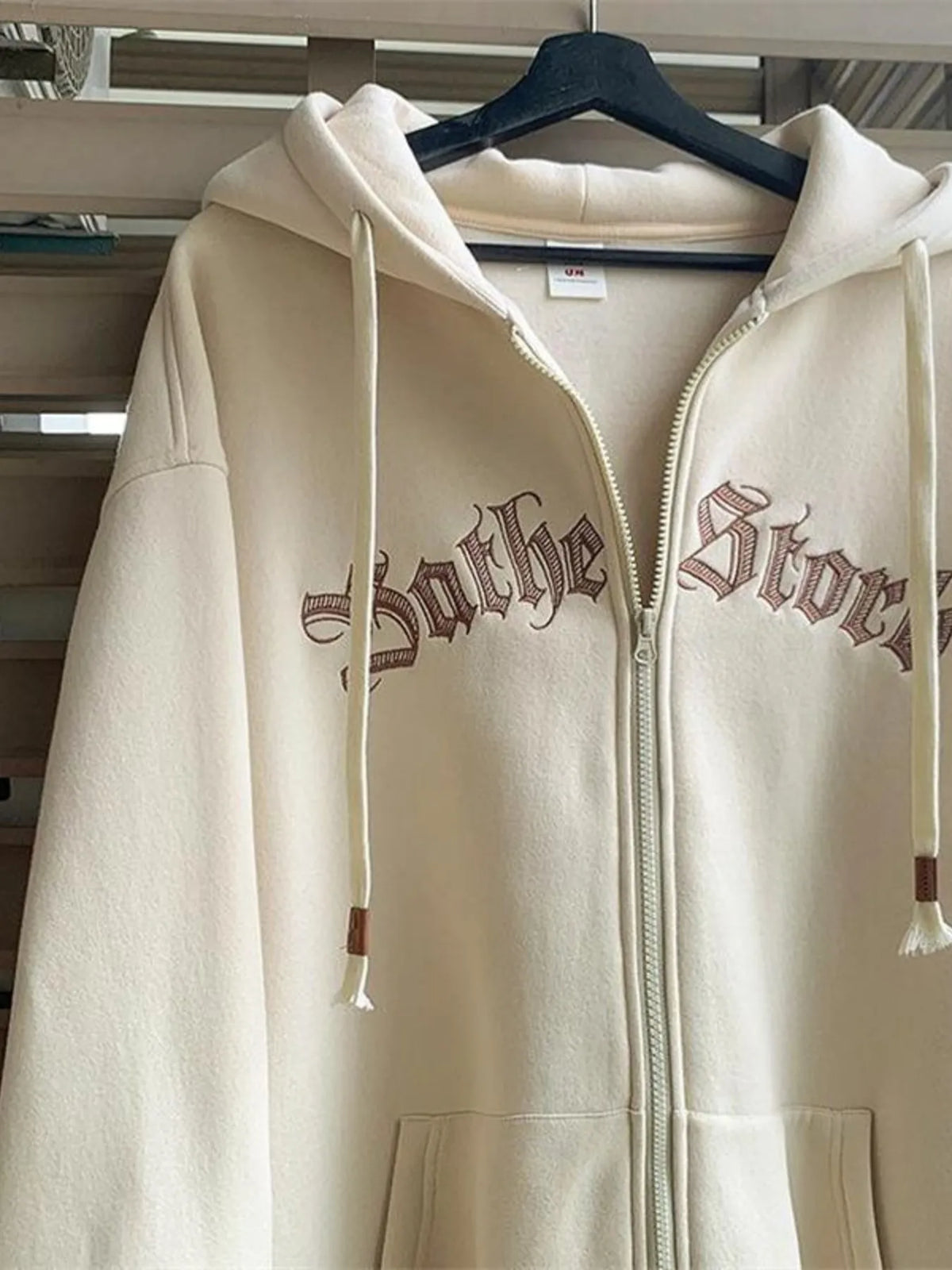 Apricot zip up hoodie with drawstrings and gothic text embroidery.