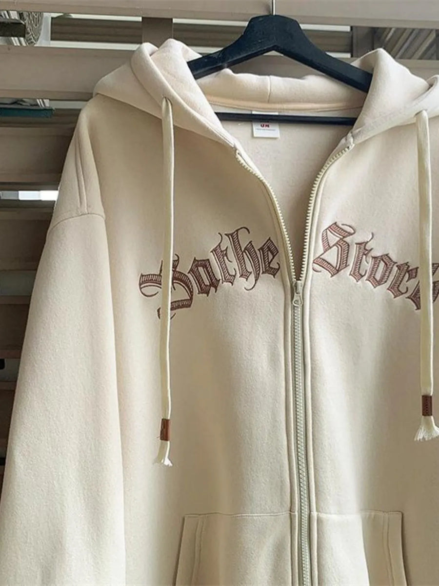 Apricot zip up hoodie with drawstrings and gothic text embroidery.