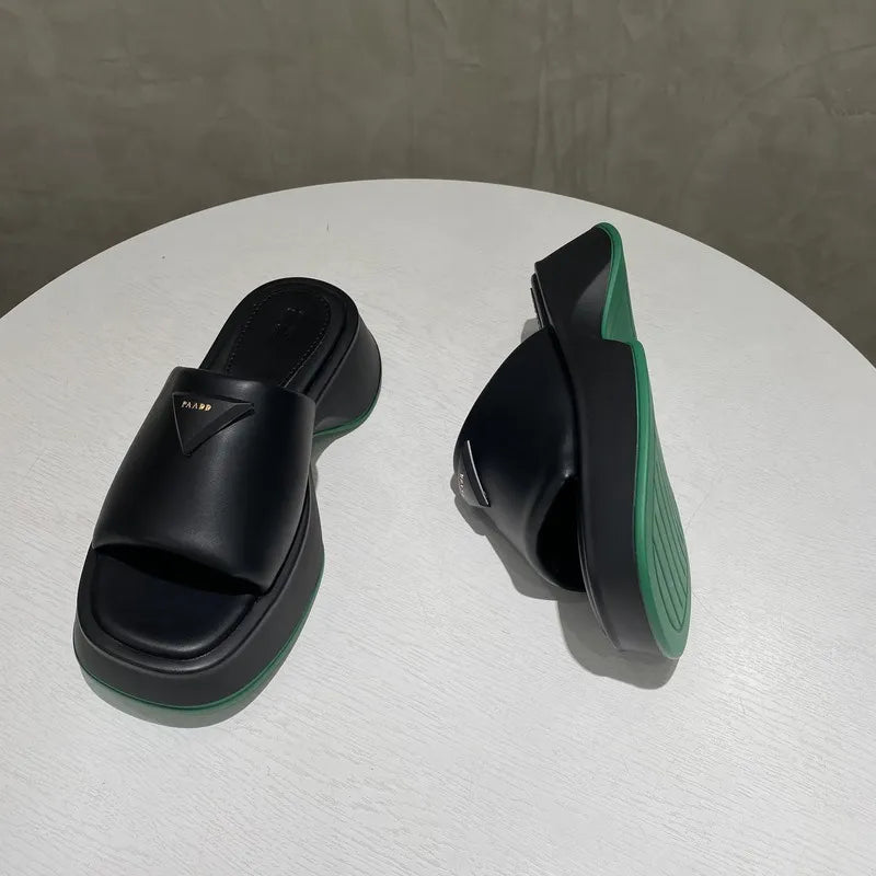 Black geometric platform slides with green sole and triangle logo detail.