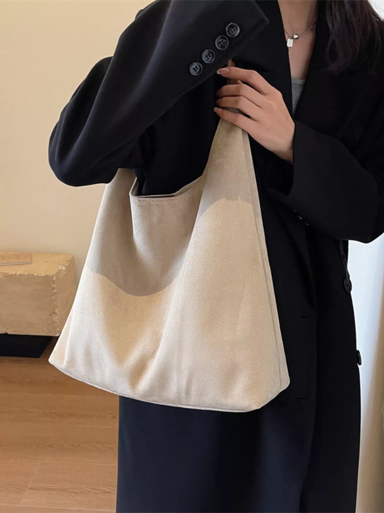 Beige suede shoulder bag with a slouchy silhouette and exterior pocket.