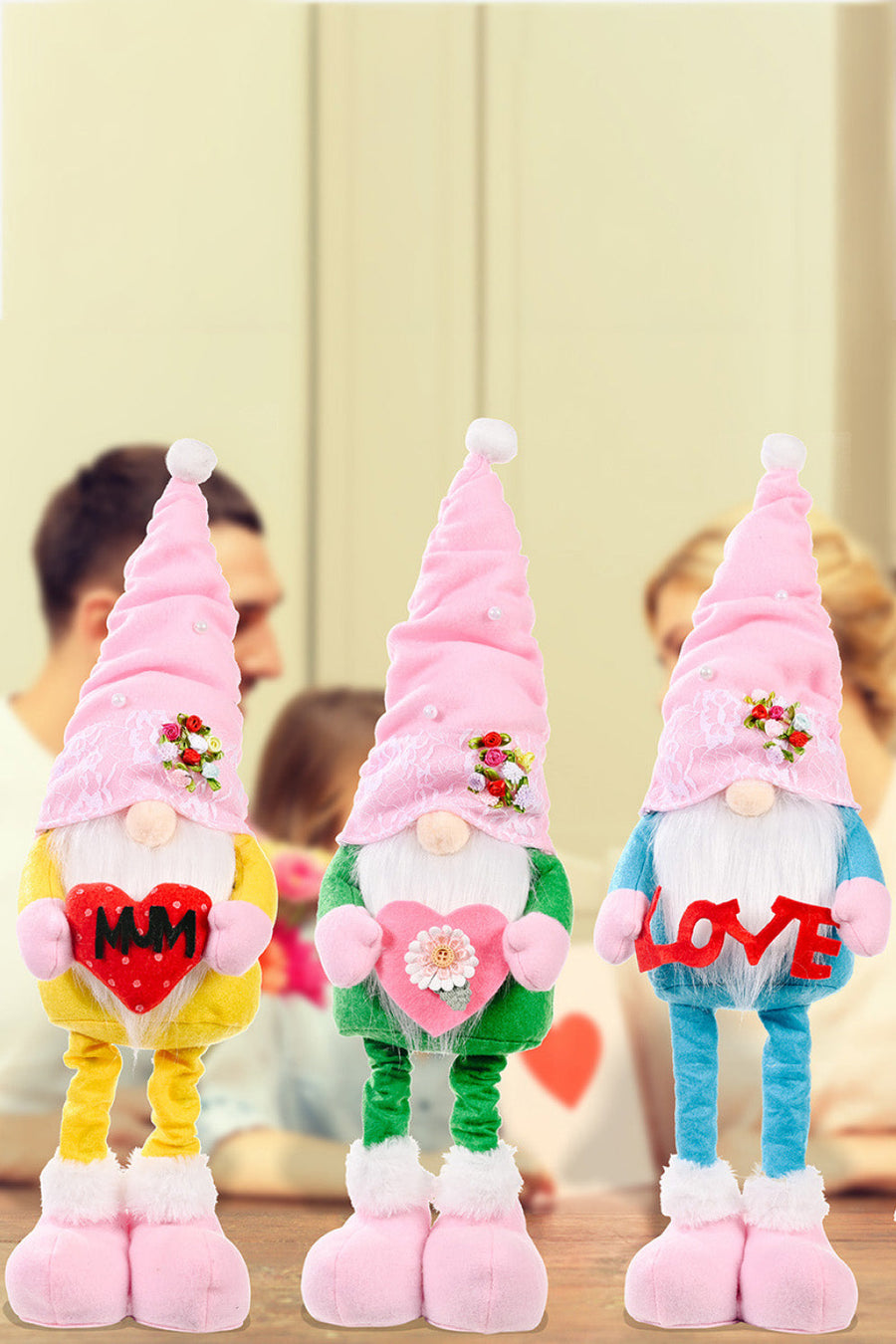 Three garden gnomes in yellow, green, and sky blue holding heart decorations.