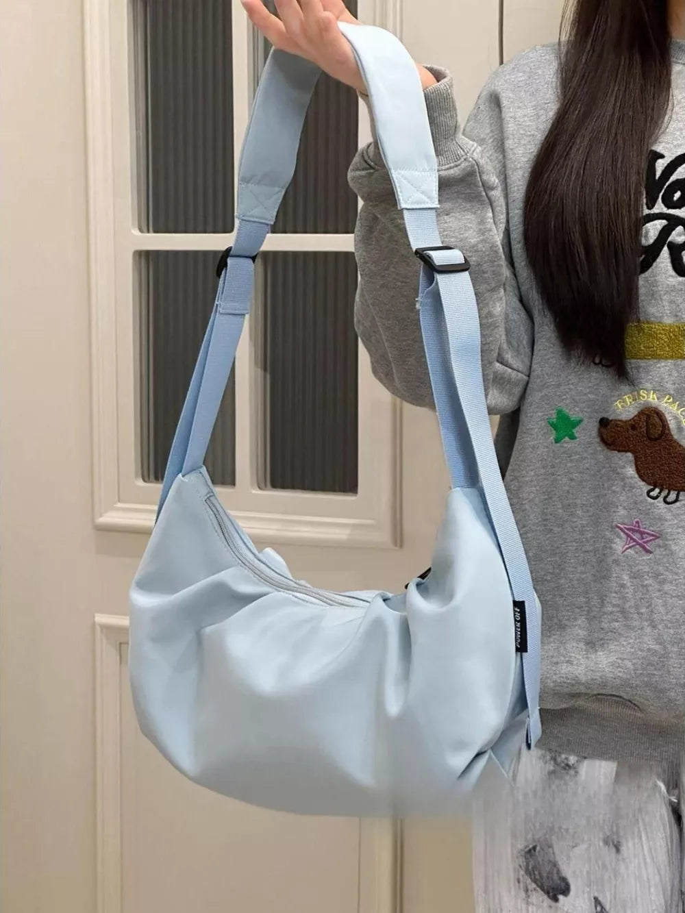 Light blue crescent shape crossbody bag with adjustable strap and zipper closure.