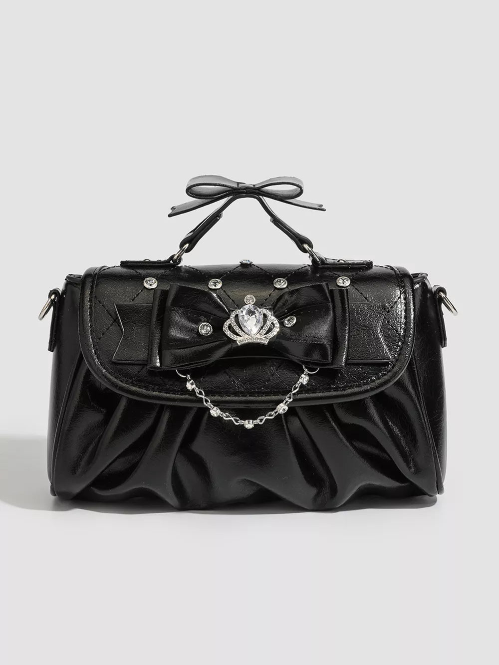 Black ruched crossbody bag with bow, crown charm, and chain detail.