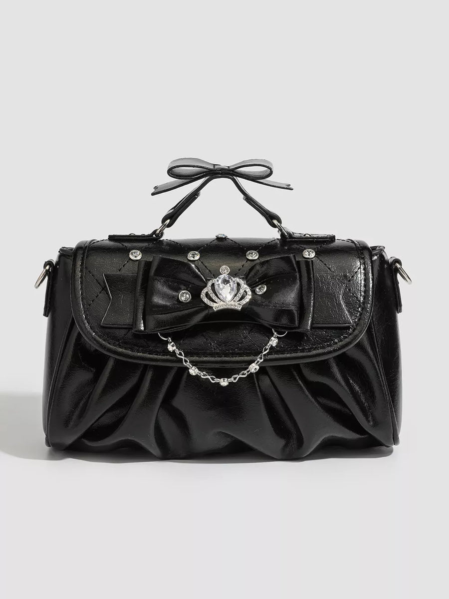 Black ruched crossbody bag with bow, crown charm, and chain detail.