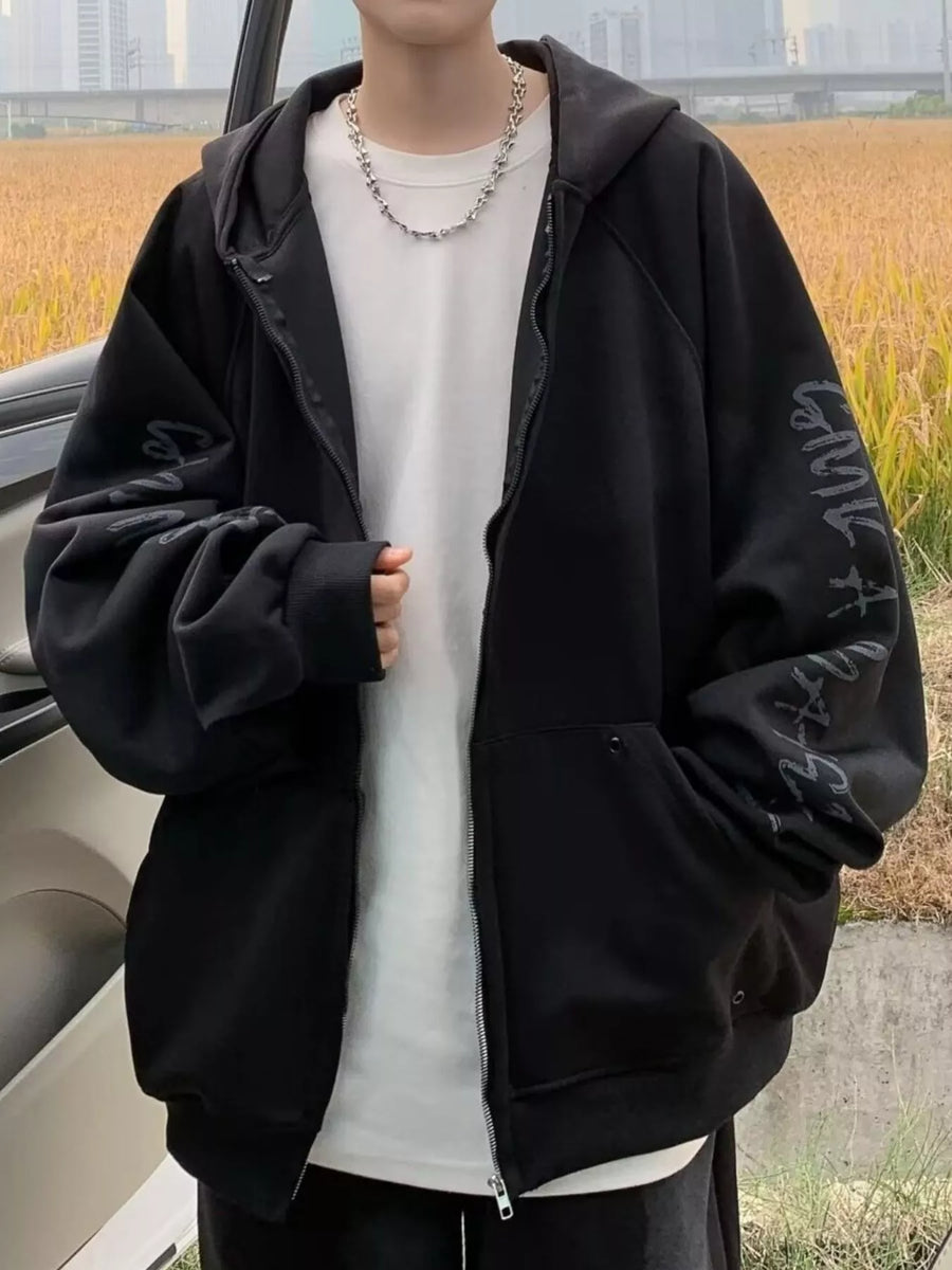Black oversized zip-up hoodie with graphic print on sleeve, worn by a man.
