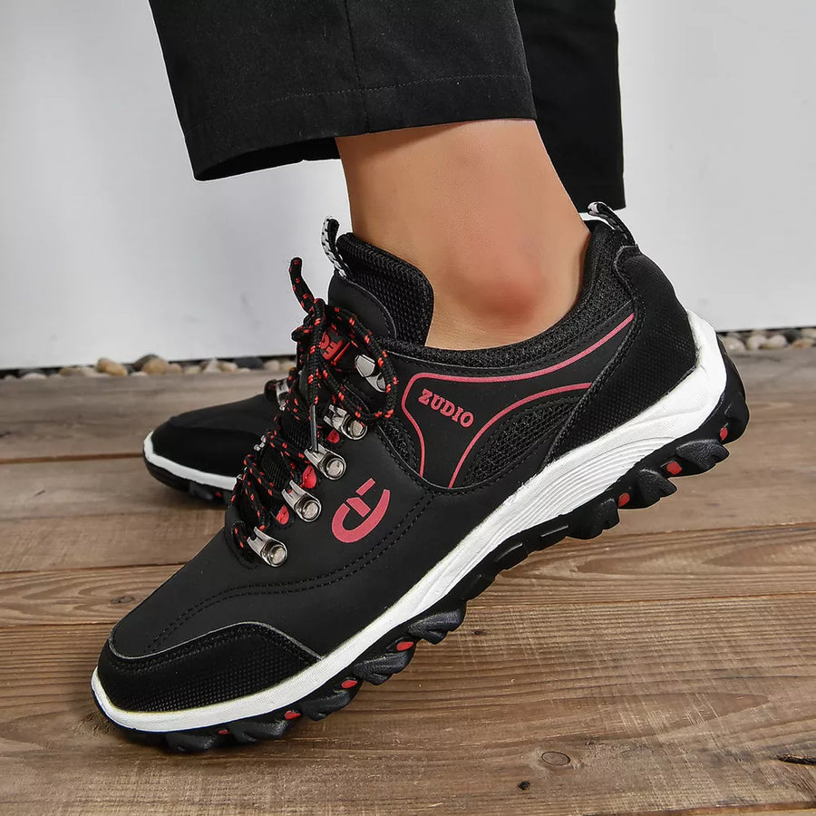 Black low-top sneakers with patterned red laces and pink accents.
