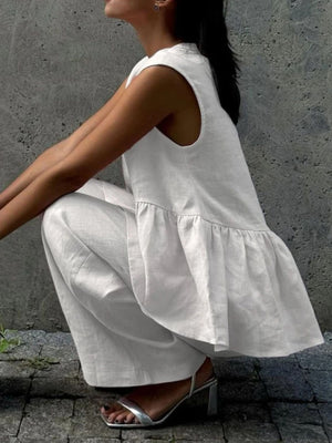 White sleeveless peplum top and wide-leg pants set in cotton, styled with silver heels.