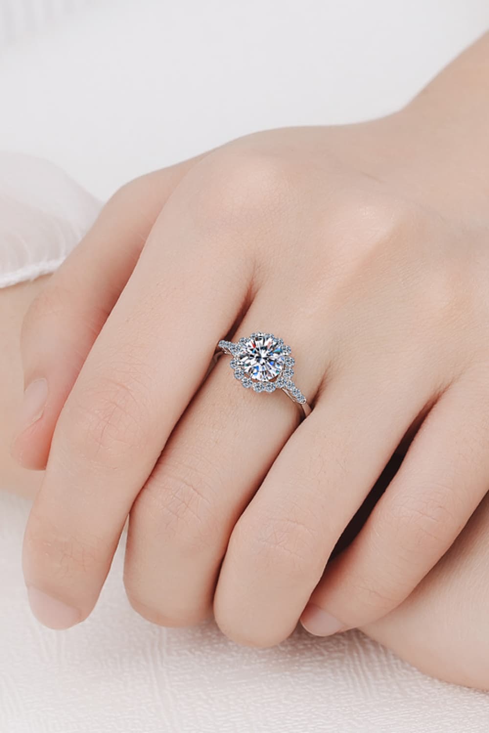 Silver halo cluster moissanite engagement ring with a round center stone and pavé band.