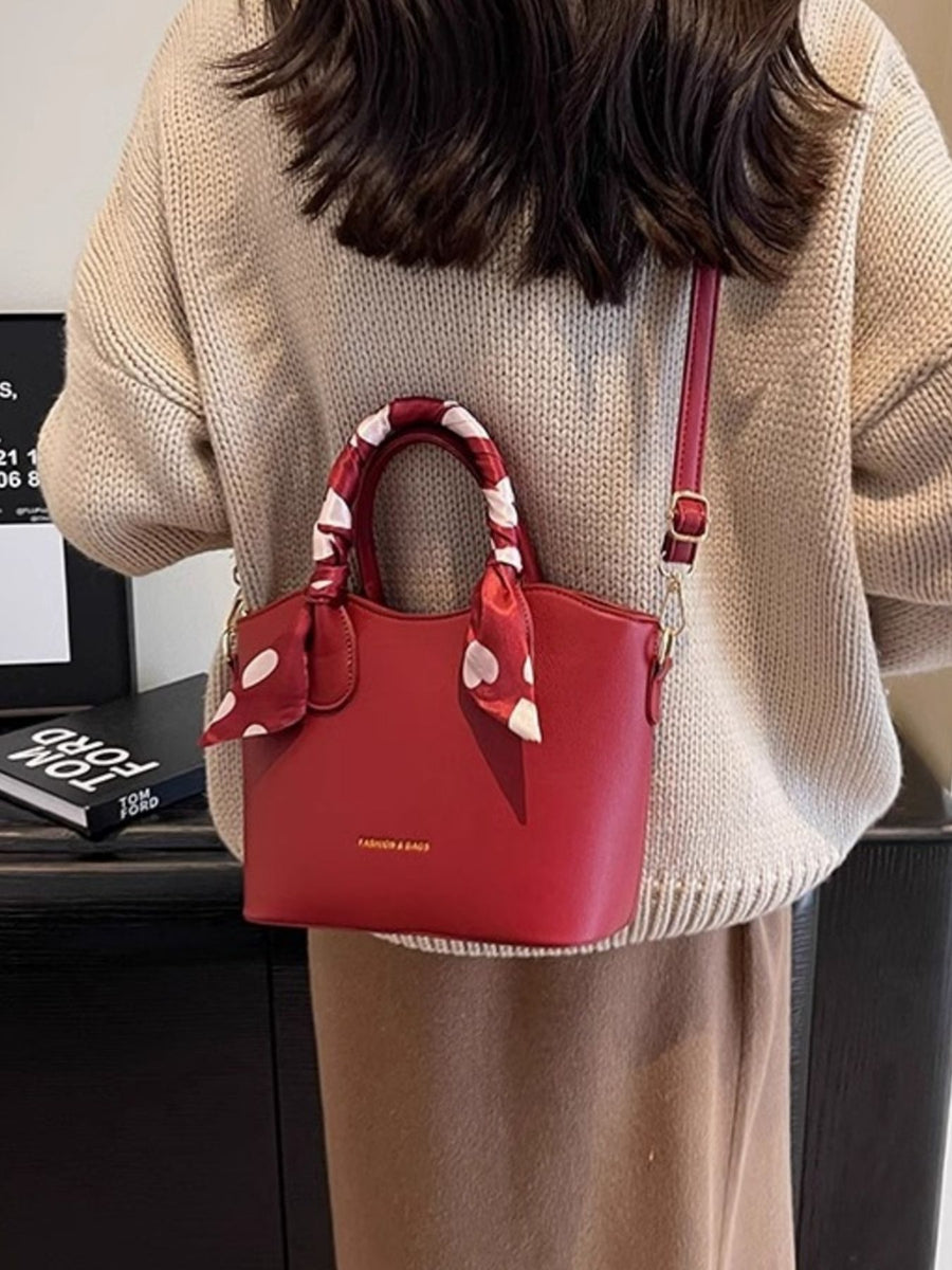 Red pu leather bucket bag with polka dot scarf detail and adjustable strap.
