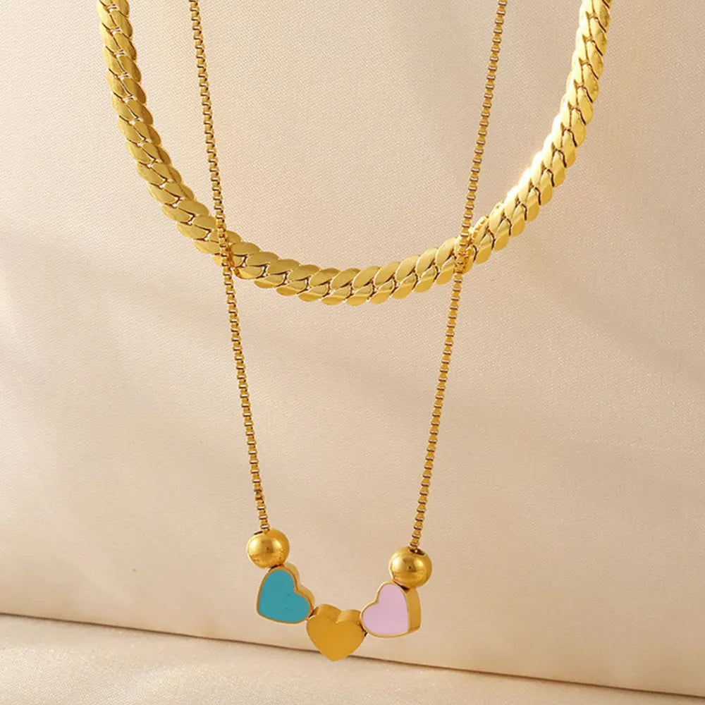 Gold double layered necklace with a flat herringbone chain and a delicate box chain featuring colorful heart charms.