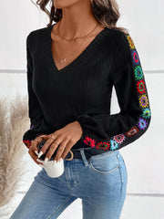 Black ribbed knit v-neck blouse with colorful embroidered sleeves and cuffs.