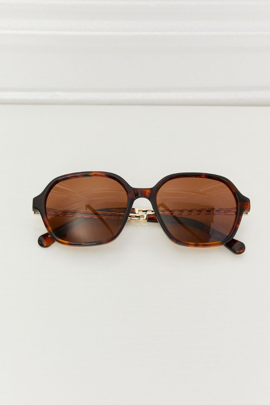Tortoiseshell hexagonal frame sunglasses with brown lenses and gold chain detail