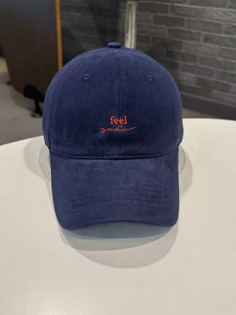 Navy baseball cap with red embroidered "feel" text and curved brim