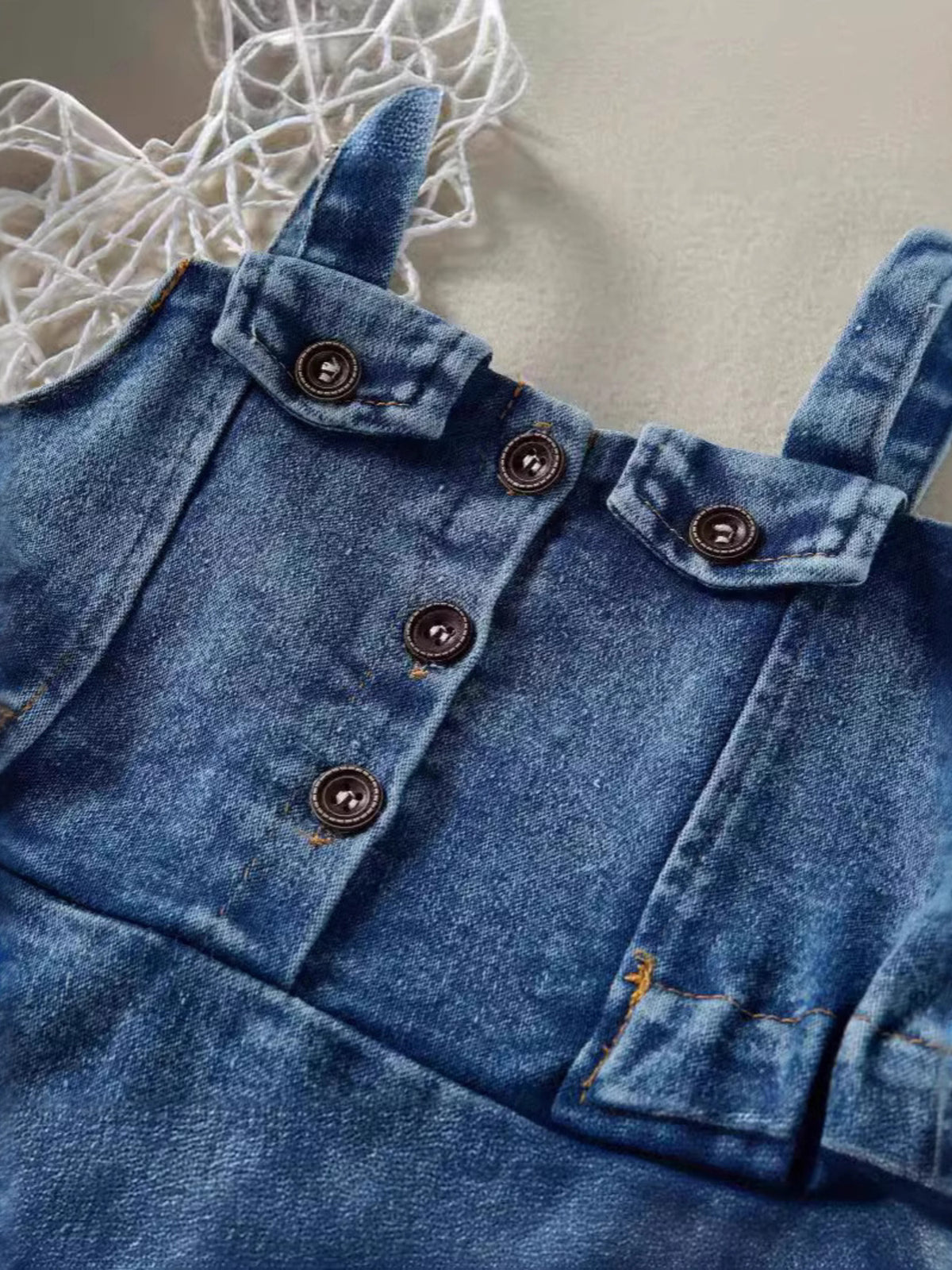 Adjustable denim overall dress for kids with button-down front and pocket details.