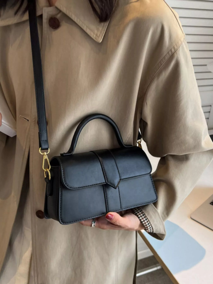 Chic small black top handle shoulder bag with gold hardware and a flap closure.