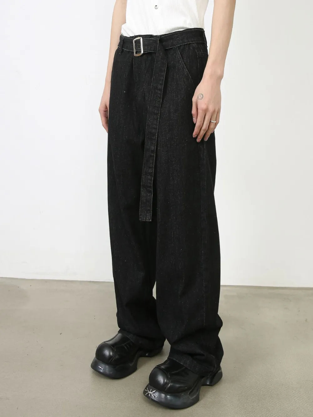 Black denim wide-leg trousers with a belted waist and sculptural silhouette.