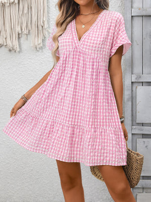 Pink gingham V-neck mini dress with tiered ruffle hem and short sleeves.