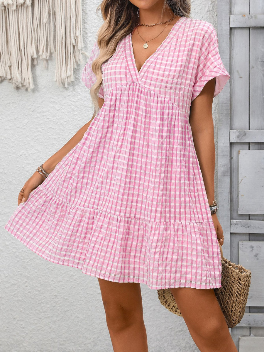Pink gingham V-neck mini dress with tiered ruffle hem and short sleeves.