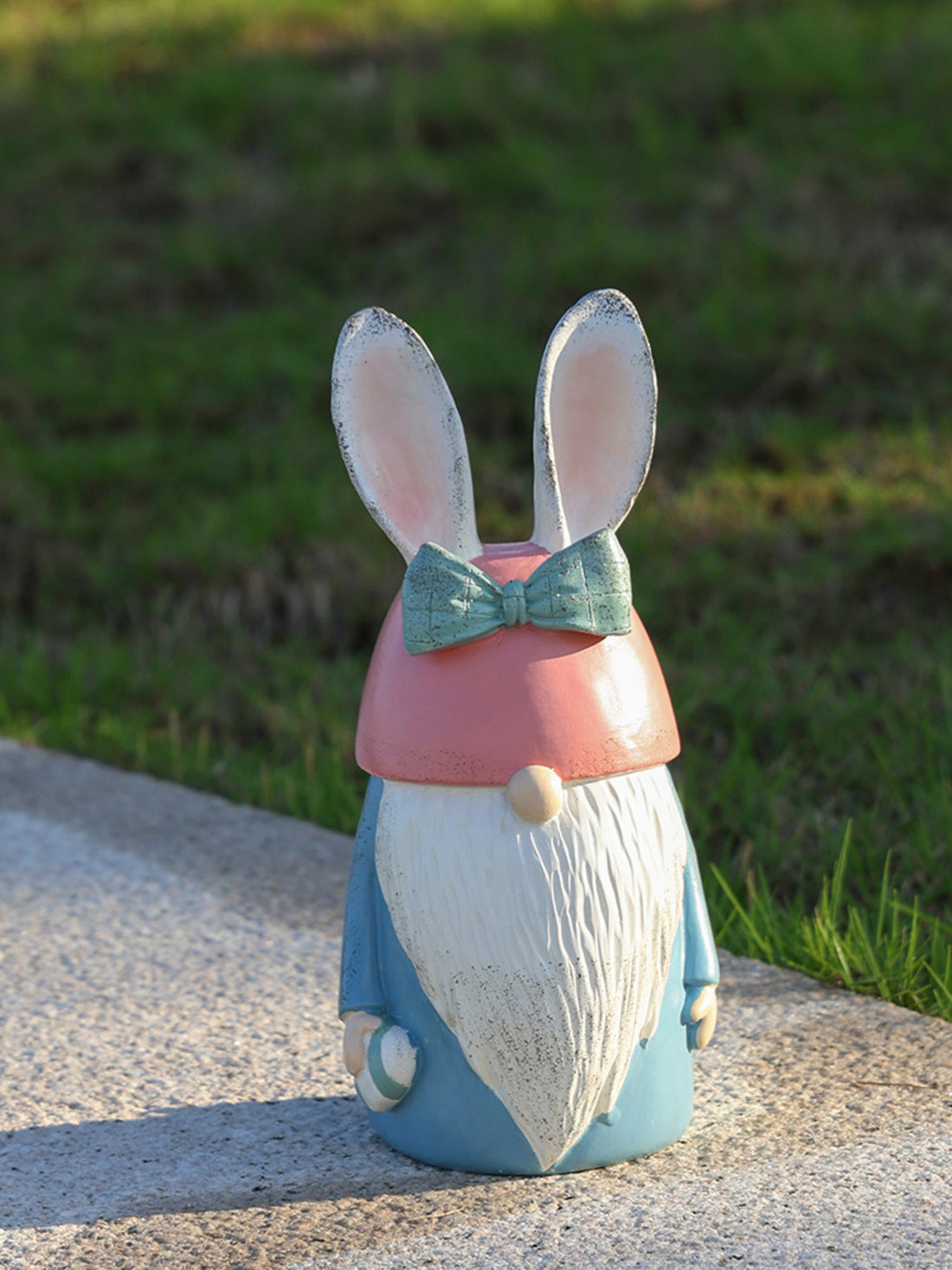 Easter bunny gnome in pastel blue with pink hat and green bow tie, holding an egg.