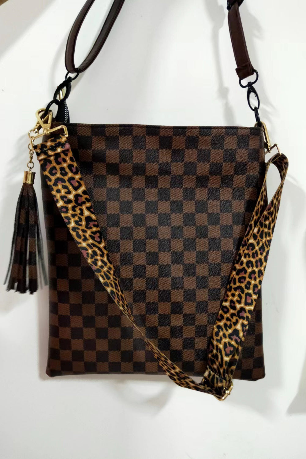 Chocolate crossbody bag with checkerboard print, leopard strap, and tassel detail.