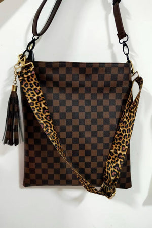 Chocolate crossbody bag with checkerboard print, leopard strap, and tassel detail.
