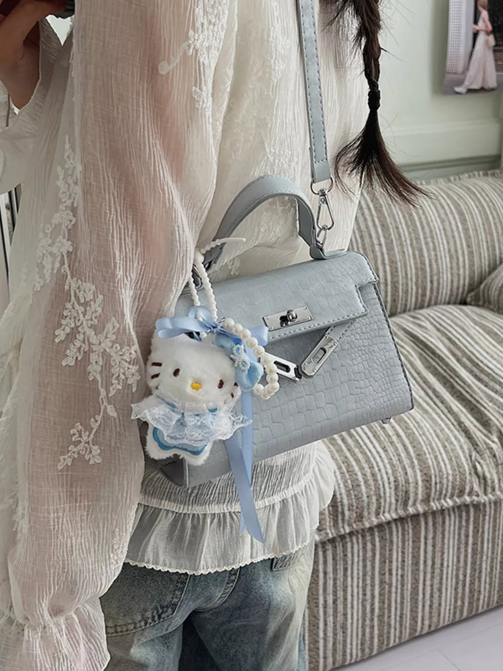 Pastel blue croc-embossed mini crossbody bag with a Hello Kitty charm and pearl strap detail.