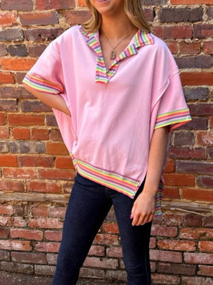 Pink cotton V-neck top with rainbow striped collar and cuffs, relaxed fit, exposed seams.